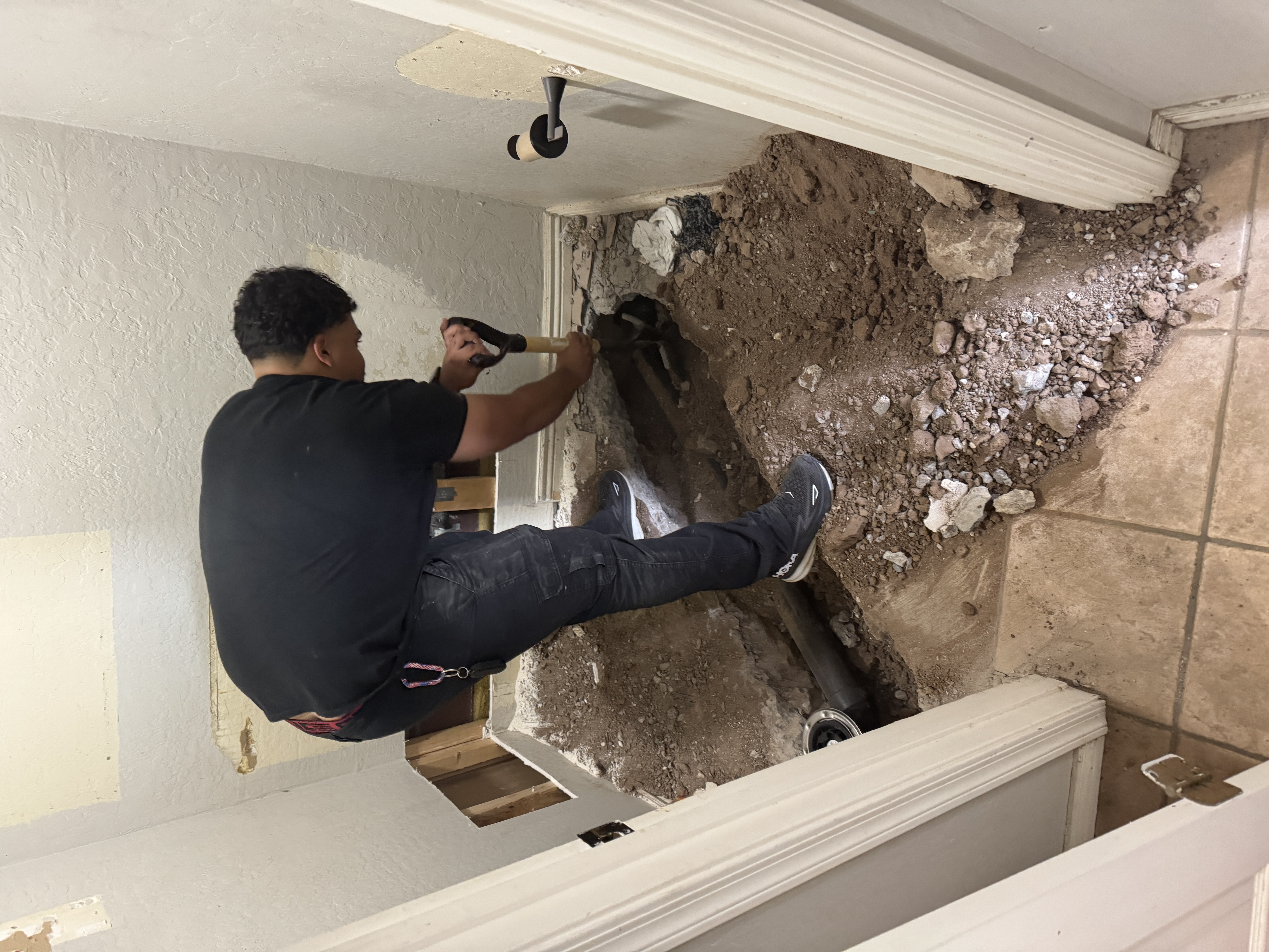 Plumber performing excavation-style drain or sewer repair inside a bathroom floor