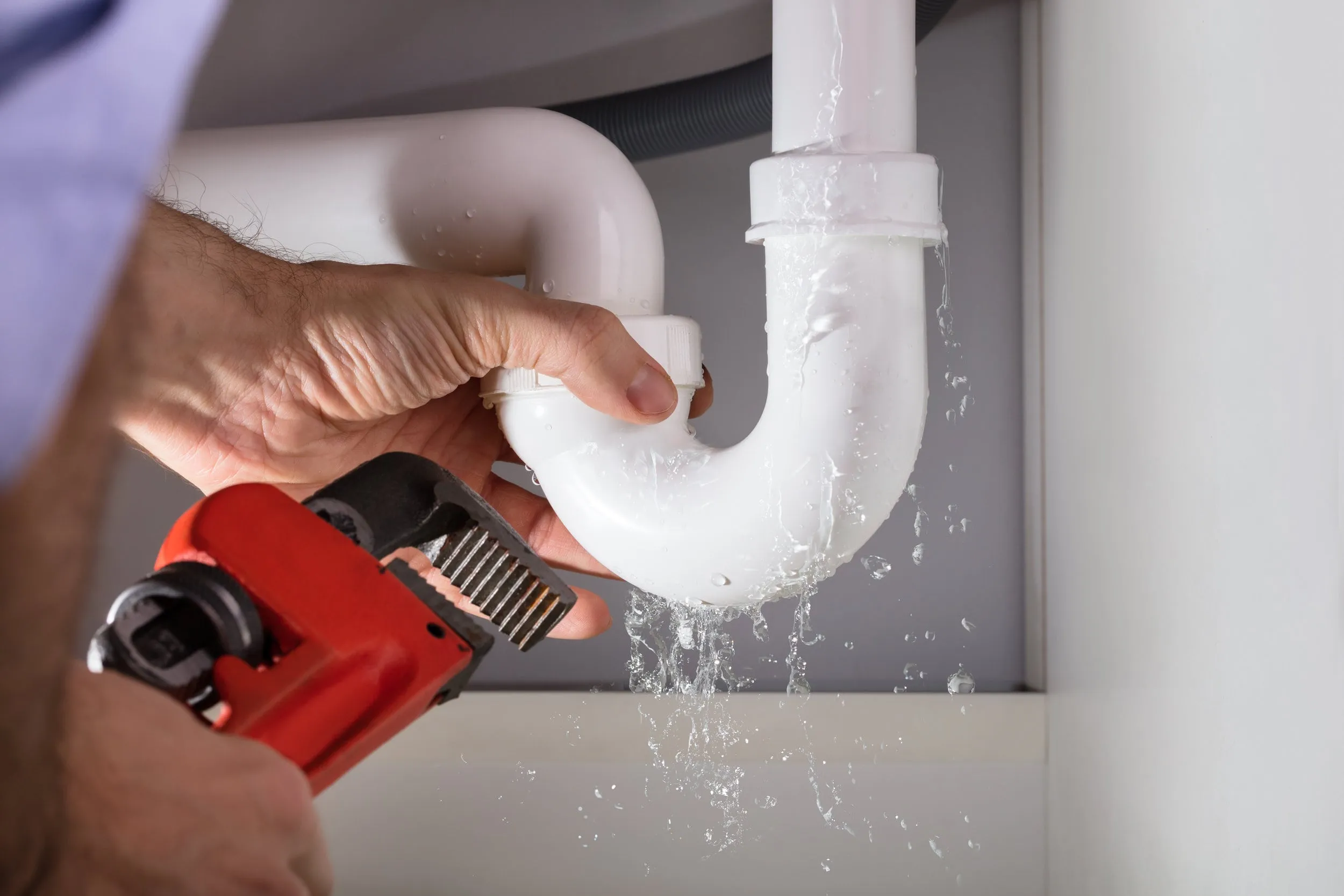 Leaking drain pipe being repaired with a pipe wrench